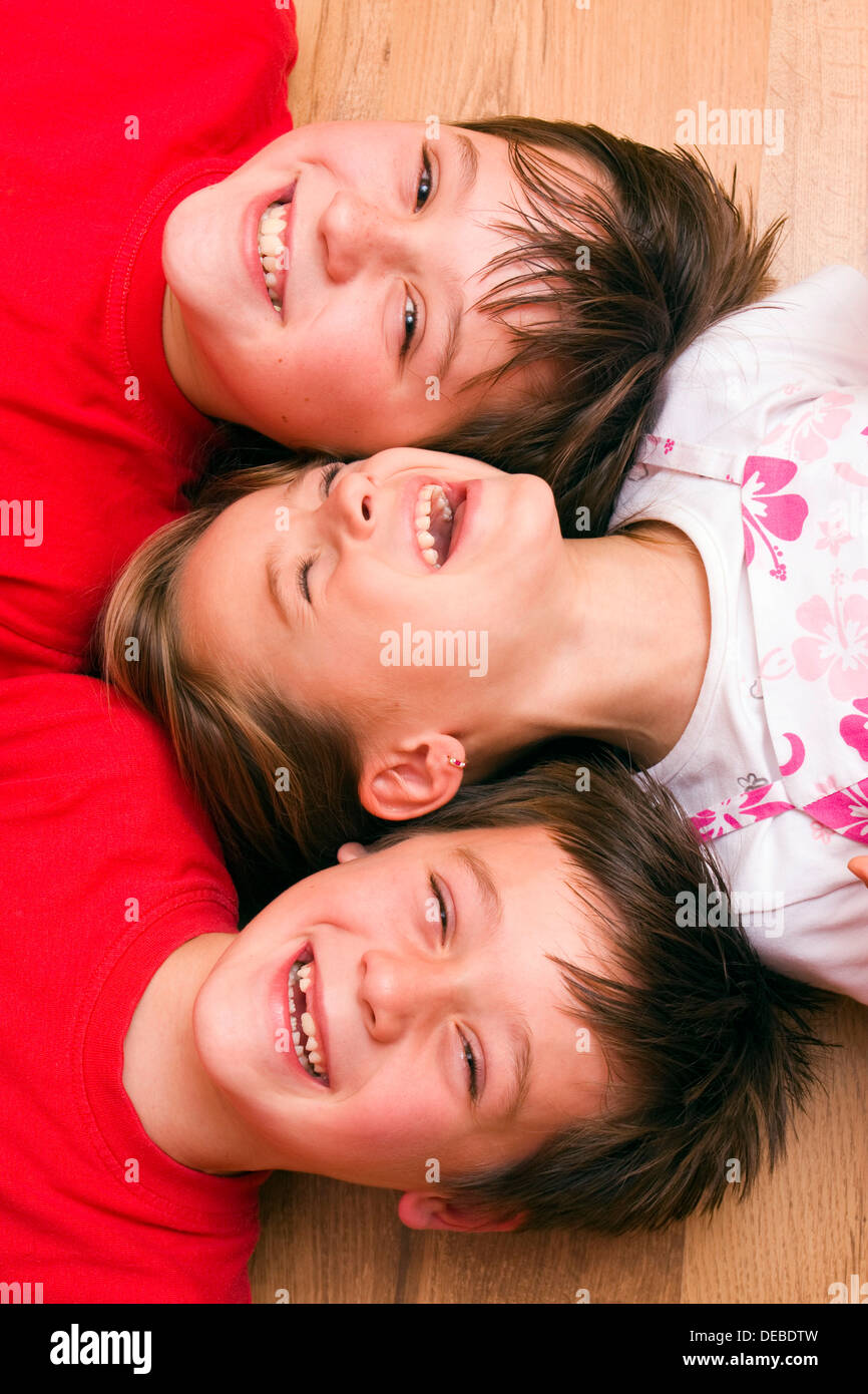 Ragazza 4 anni, e i ragazzi di 6 e 11 anni, sdraiato sul pavimento, ridendo Foto Stock