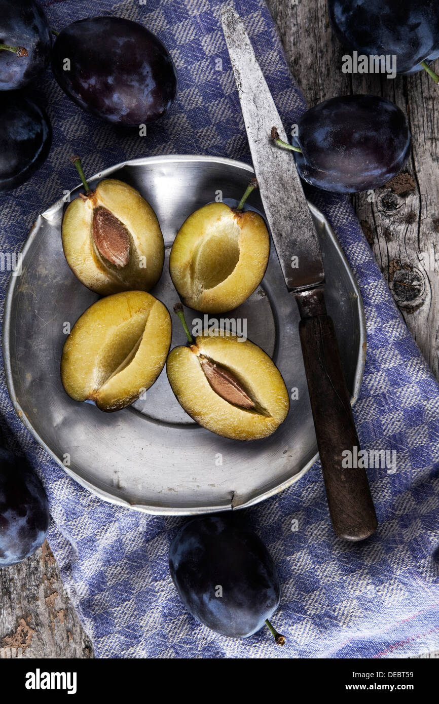 Prugne fresche (Prunus domestica) su una piastra dello stagno, con la lama di un coltello e un asciugamano da cucina Foto Stock