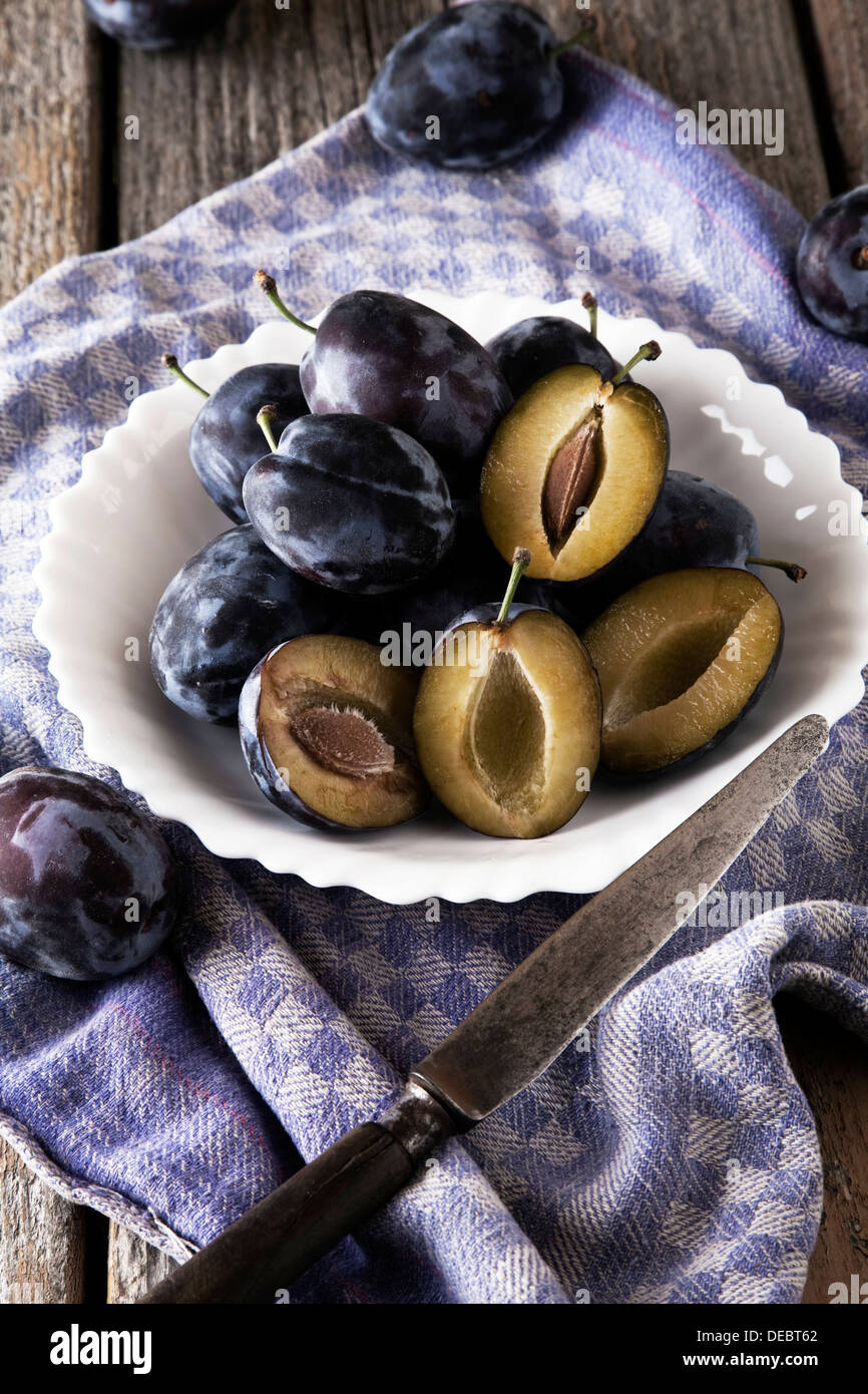 Prugne fresche (Prunus domestica) sulla piastra, con la lama di un coltello e un asciugamano da cucina Foto Stock