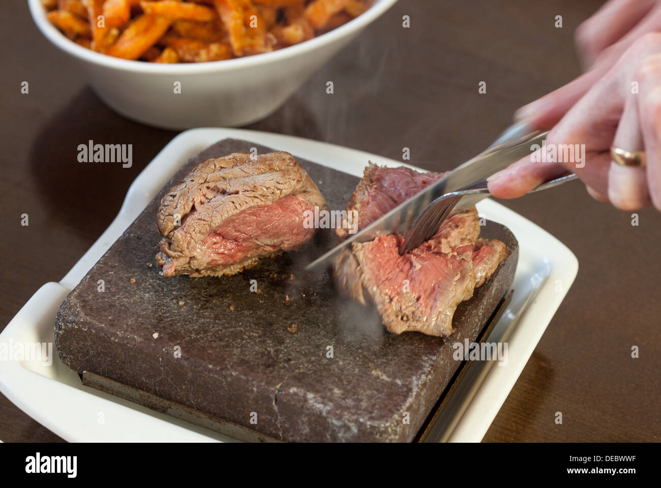 Bistecca sfrigolante su pietra calda piastra essendo tagliate a fette Foto Stock