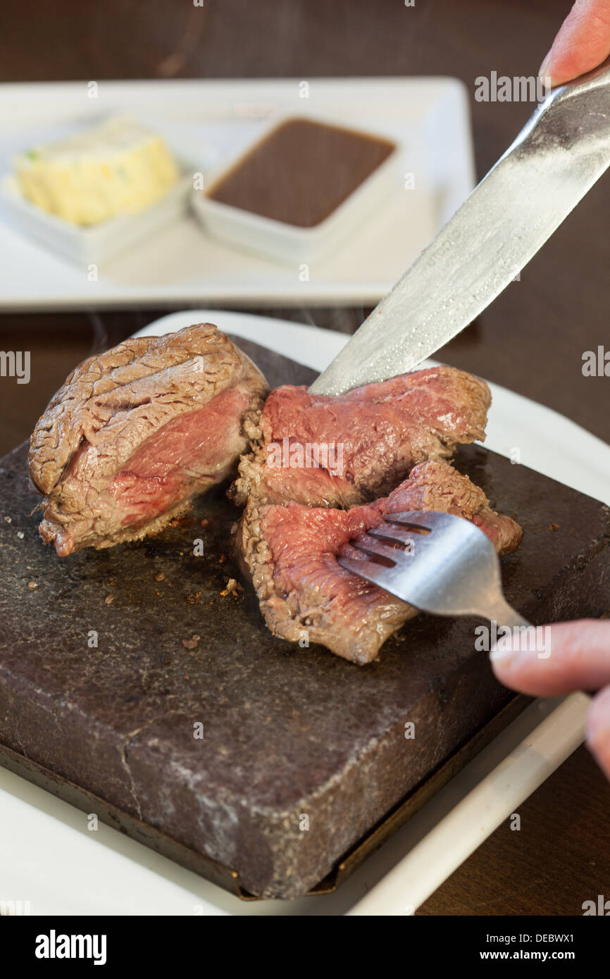 Mezzo raro bistecca sfrigolante su pietra calda piastra essendo tagliate a fette Foto Stock