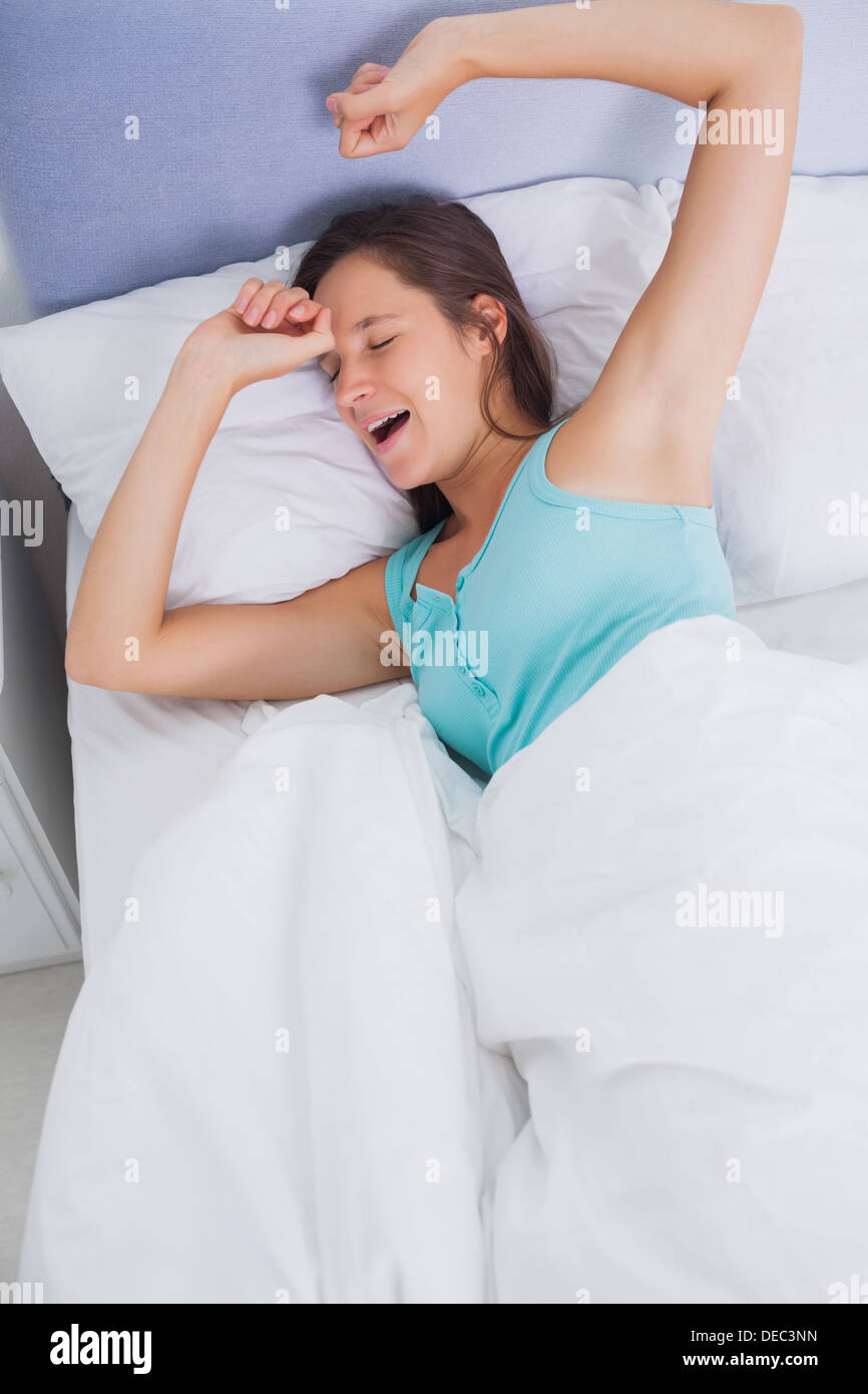 Ben riposati brunette donna stretching e sbadigli nel letto Foto Stock