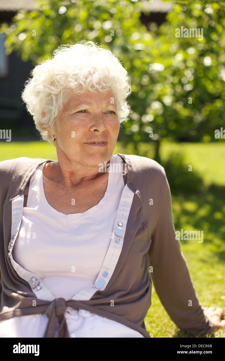 Ritratto di rilassata vecchia signora seduta su erba che guarda lontano - all'aperto Foto Stock