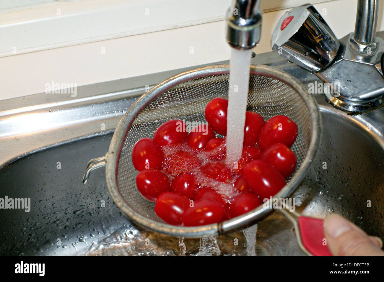 Rossi pomodori ciliegini essendo lavate sotto acqua corrente Foto Stock