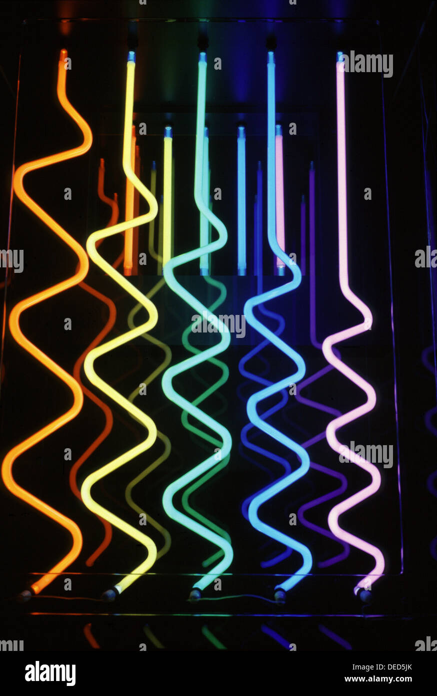 Diversi tubi luminosi al neon ondulati disposti verticalmente, ciascuno dei quali è illuminato in un colore diverso, tra cui arancione, giallo, turchese, blu, e rosa. Foto Stock