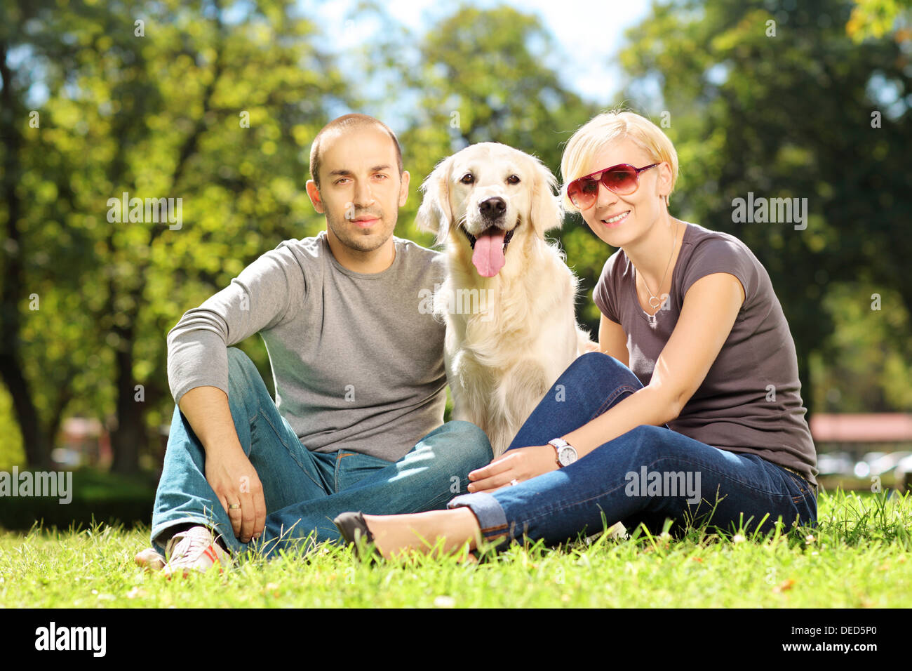 Sorridente coppia giovane abbracciando un cane in un parco Foto Stock