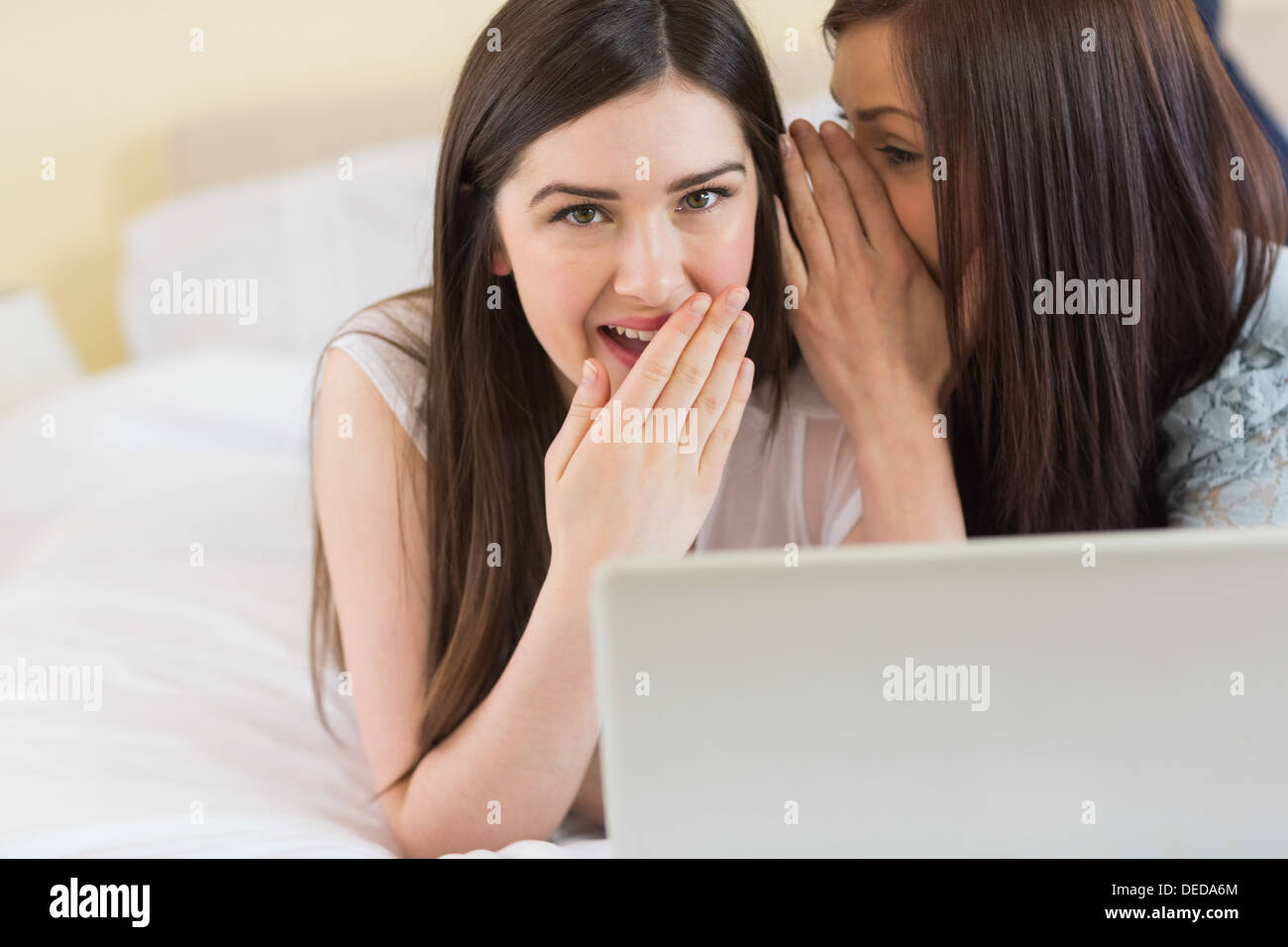 Felice ragazza raccontando un segreto per il suo amico nella parte anteriore del computer portatile Foto Stock