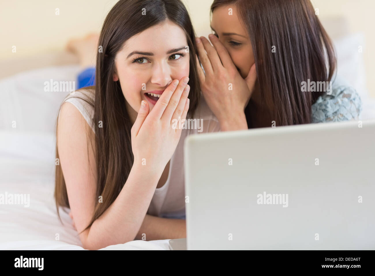 Ragazza sorridente raccontando un segreto per il suo amico nella parte anteriore del computer portatile Foto Stock