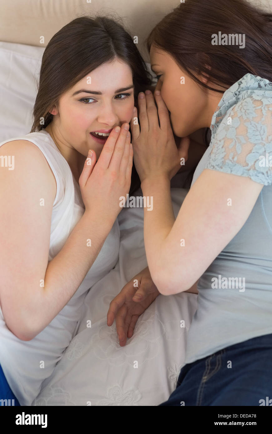 Felice ragazza raccontando un segreto al suo amico sorpreso giacente sul letto Foto Stock