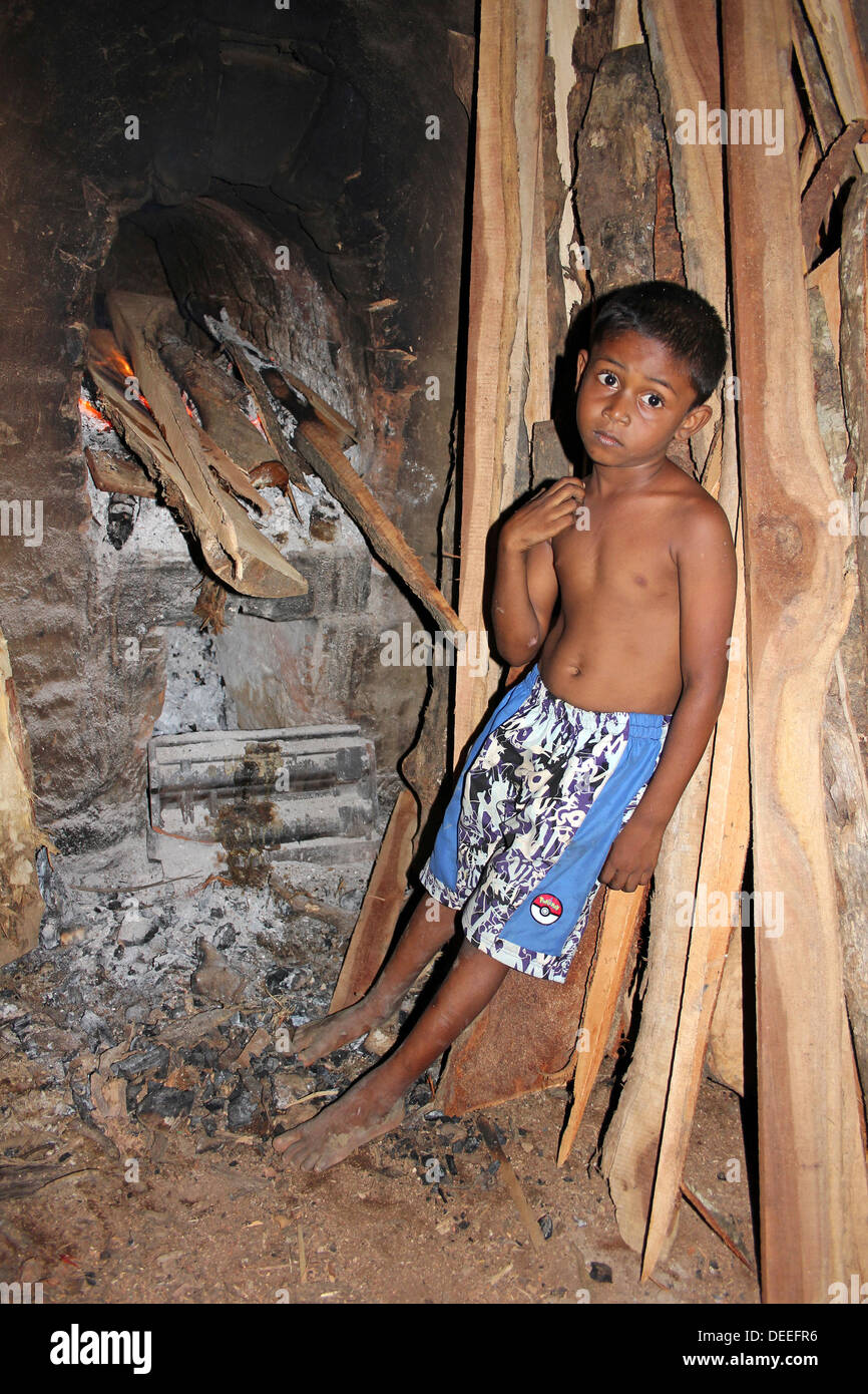 Giovane dello Sri Lanka ragazzo in piedi accanto al forno stufa in piastrelle di fabbrica Foto Stock