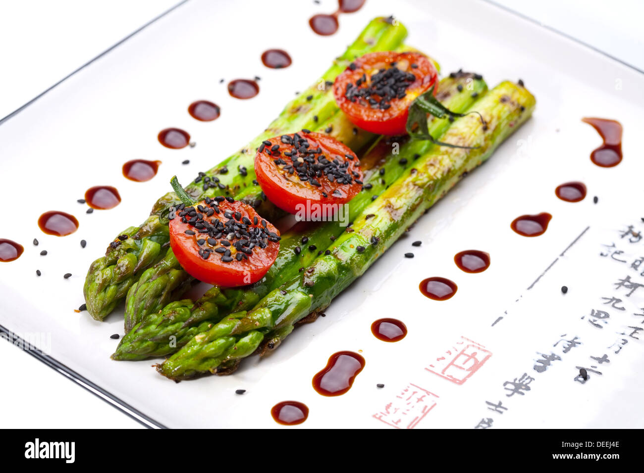 Asparagi alla griglia con pomodori su una piastra bianca. Foto Stock