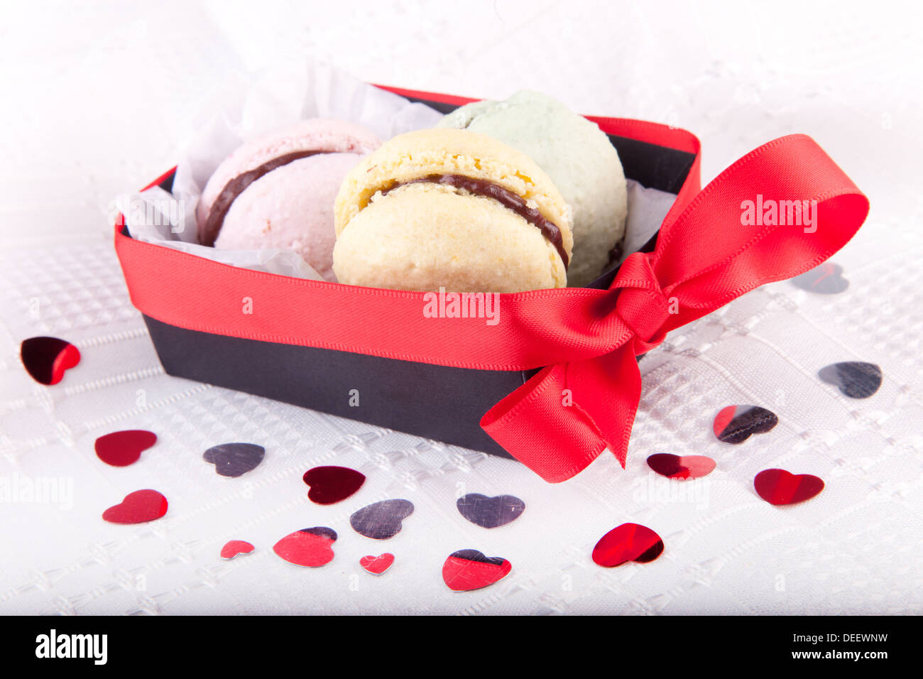 Amaretti in scatola con fiocco rosso su bianco tovaglia con cuori Foto Stock