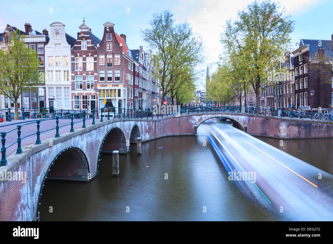 Una lunga esposizione di una imbarcazione turistica incrocio canali Keizersgracht da Leidsegracht al crepuscolo, Amsterdam, Paesi Bassi, Europa Foto Stock