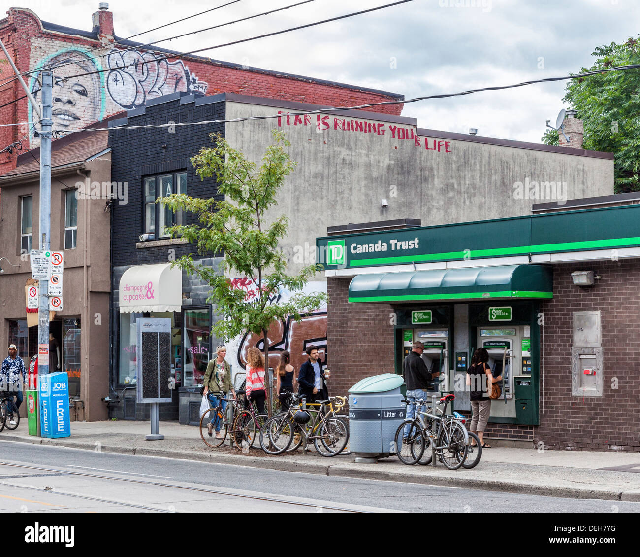 Le persone che usano ATM del Canada Trust Bank con 'è paura di rovinare la tua vita' graffiti sul muro adiacente in Queen Street West, Toronto Foto Stock