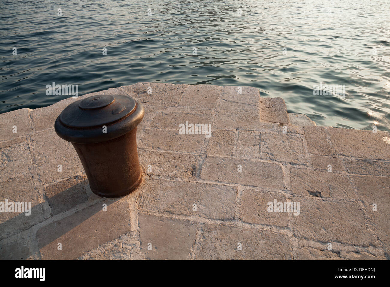 Vecchio metallo arrugginito bollard stand sul molo di pietra in Montenegro Foto Stock
