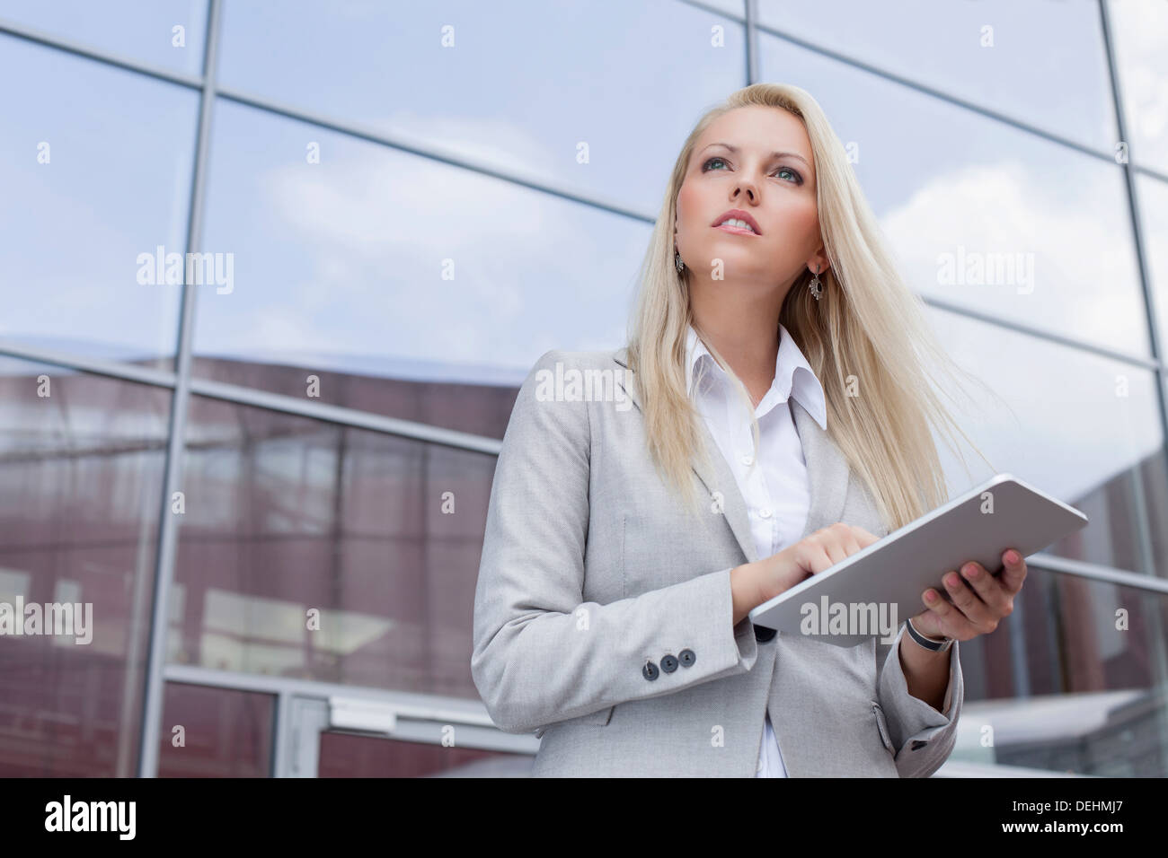 Basso angolo di visione imprenditrice azienda digitale compressa mentre guarda lontano contro l edificio per uffici Foto Stock