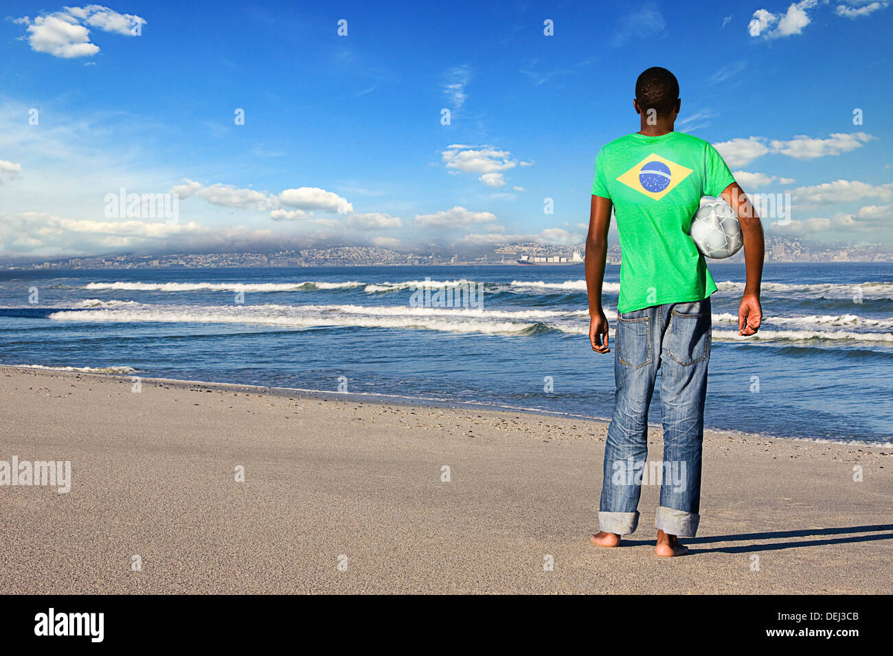 Vista posteriore man standing indossando il brasiliano t shirt con calcio su una spiaggia Foto Stock