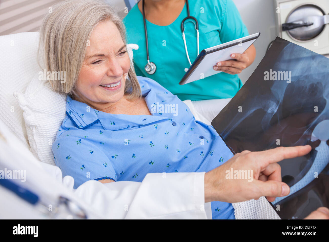 Felice donna senior il recupero del paziente nel letto di ospedale con connettore maschio di tipo medico e infermiere femmina guardando anca x-ray Foto Stock
