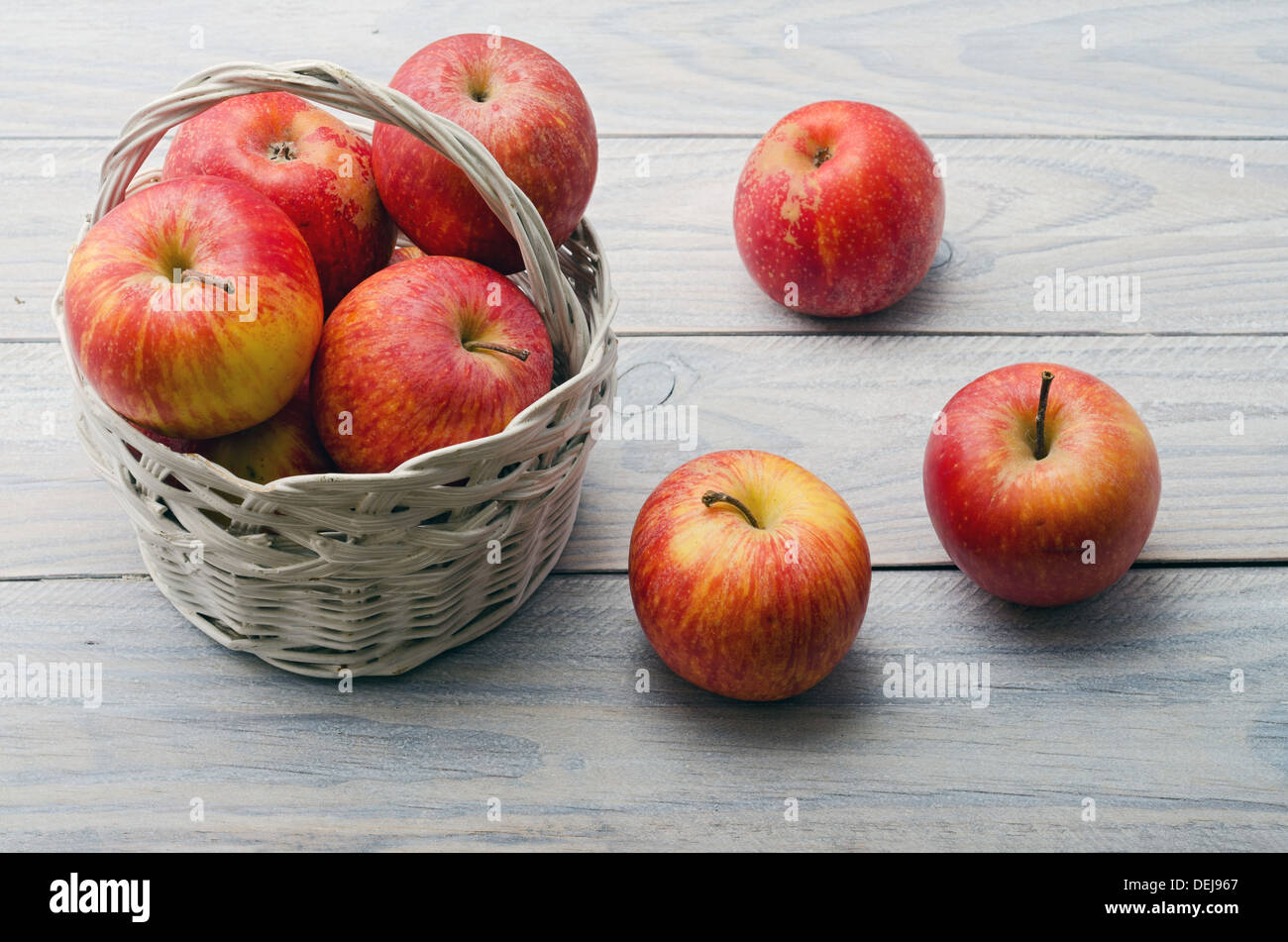Ancora in vita. Cestello di bianco con le mele rosse sul tavolo di legno bianco Foto Stock