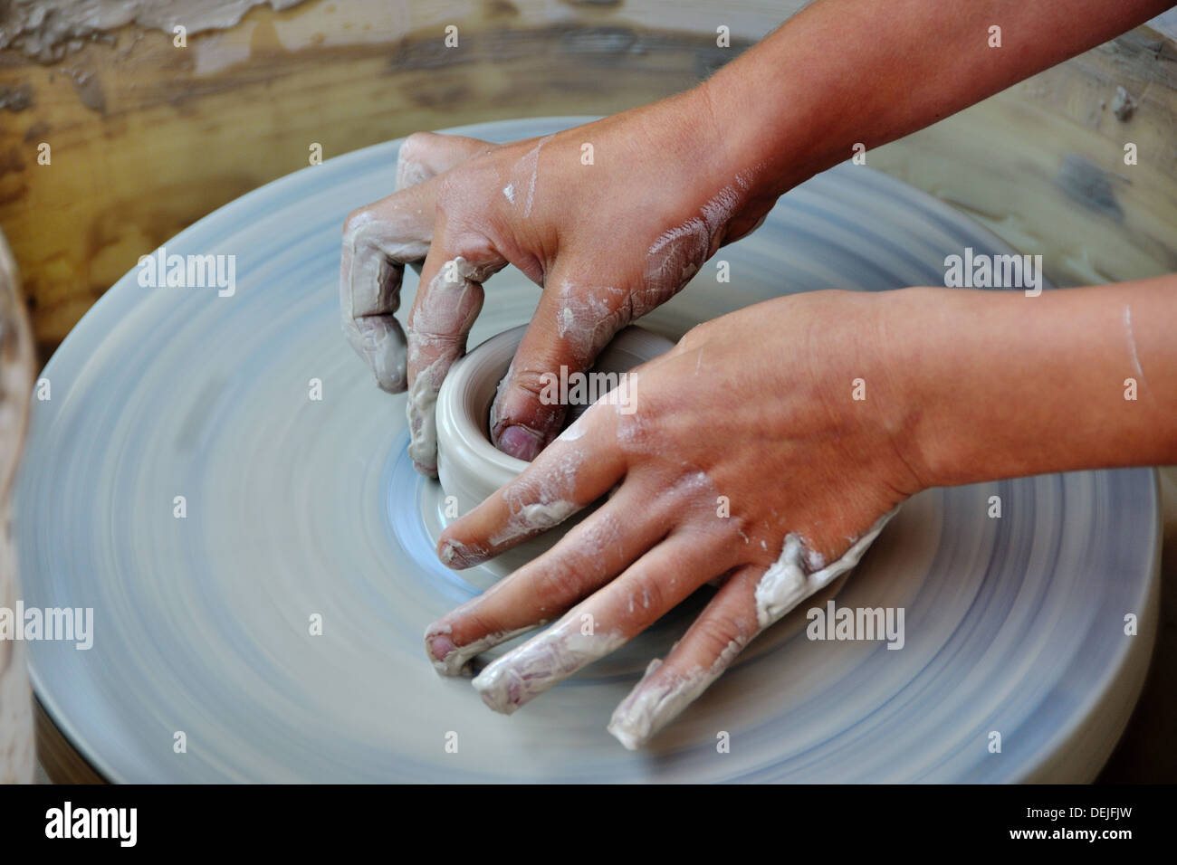 Una forma di argilla su una ceramica di filatura ruota essendo conformato da un bambino con le mani in mano. Foto Stock