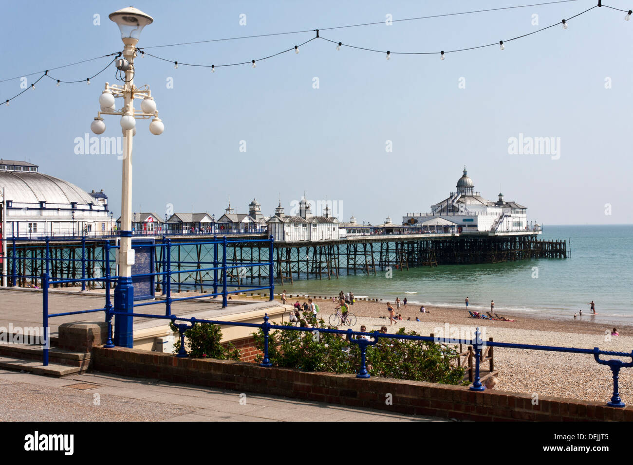 I visitatori godere il sole primaverile sulla spiaggia. Il molo a Eastbourne è un edificio classificato Grade II da English Heritage. Foto Stock