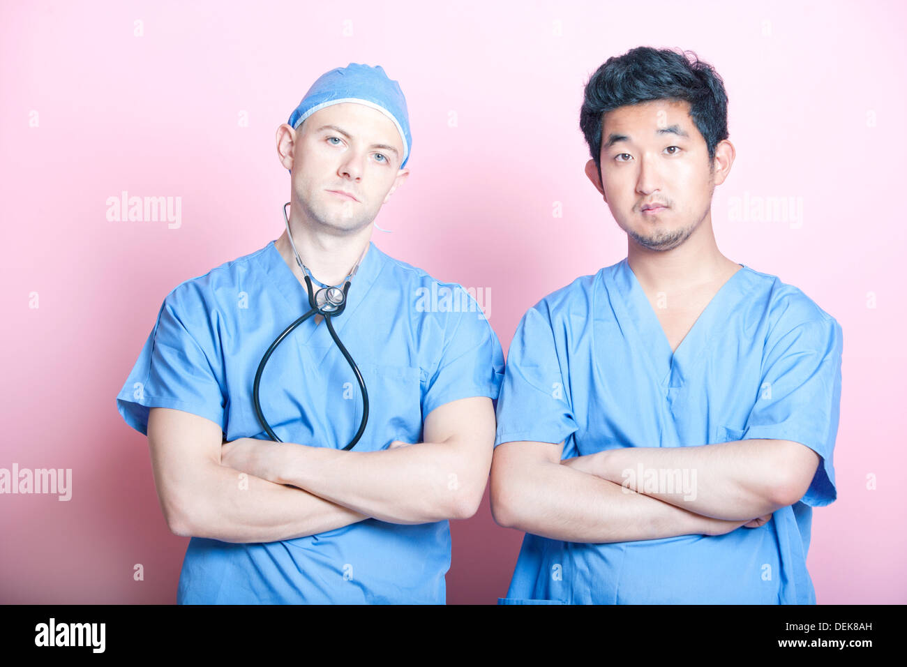 Ritratto di due chirurghi maschio in piedi con le braccia incrociate su sfondo rosa Foto Stock