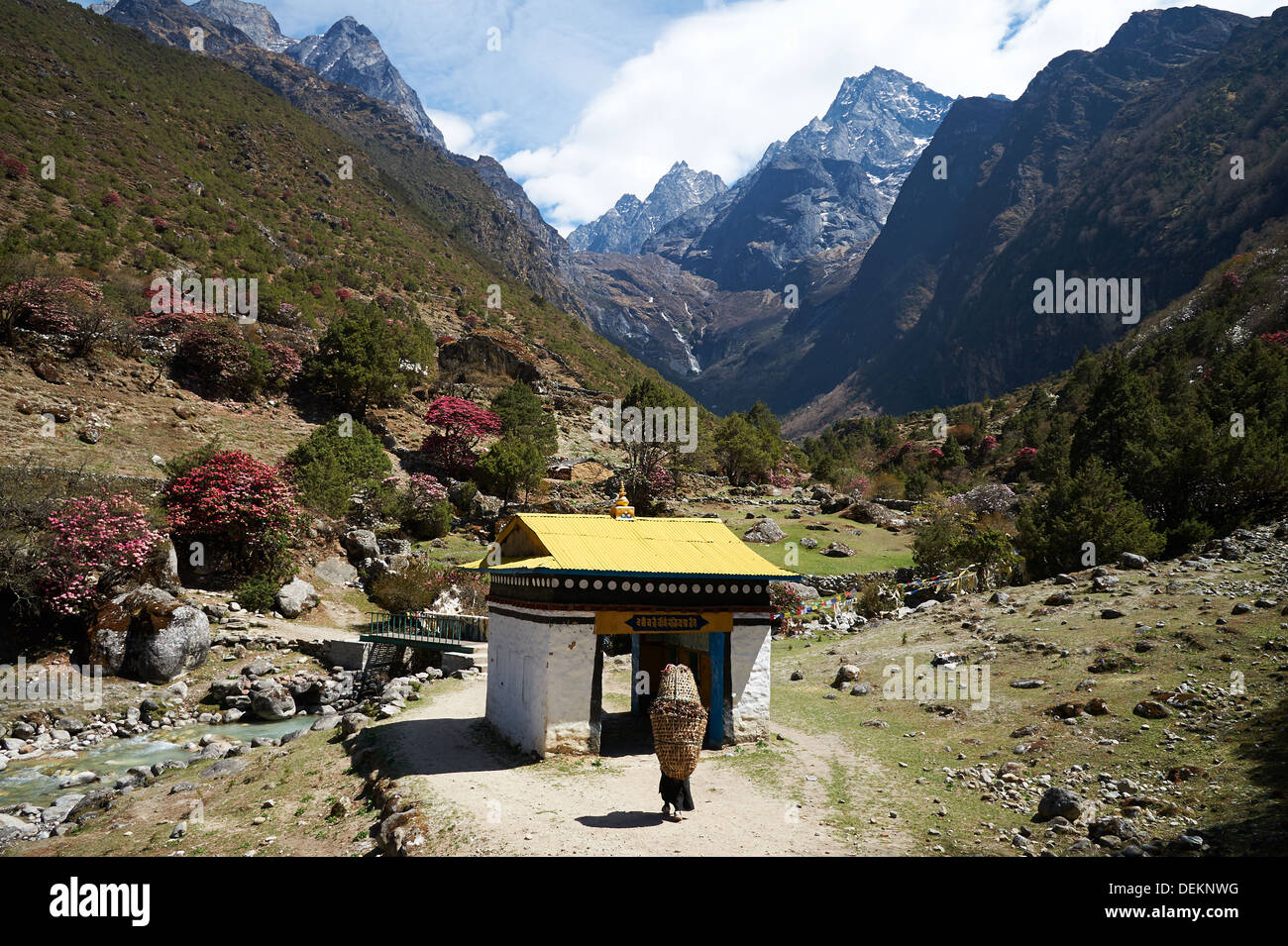 Donna Sherpa trasporta un carico pesante avvicinando una ruota di preghiera gateway sul sentiero da Namche Bazaar verso Thamo e Thame, Nepal Foto Stock