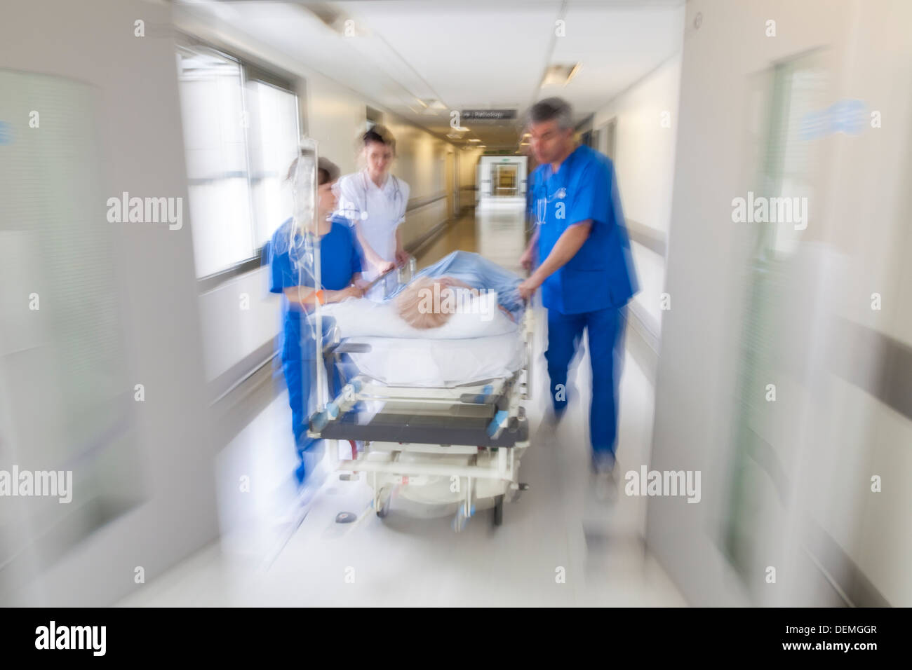 Moto foto sfocate paziente sulla barella barella spinto a velocità attraverso il corridoio ospedaliero da parte di medici e infermieri a sala di emergenza Foto Stock