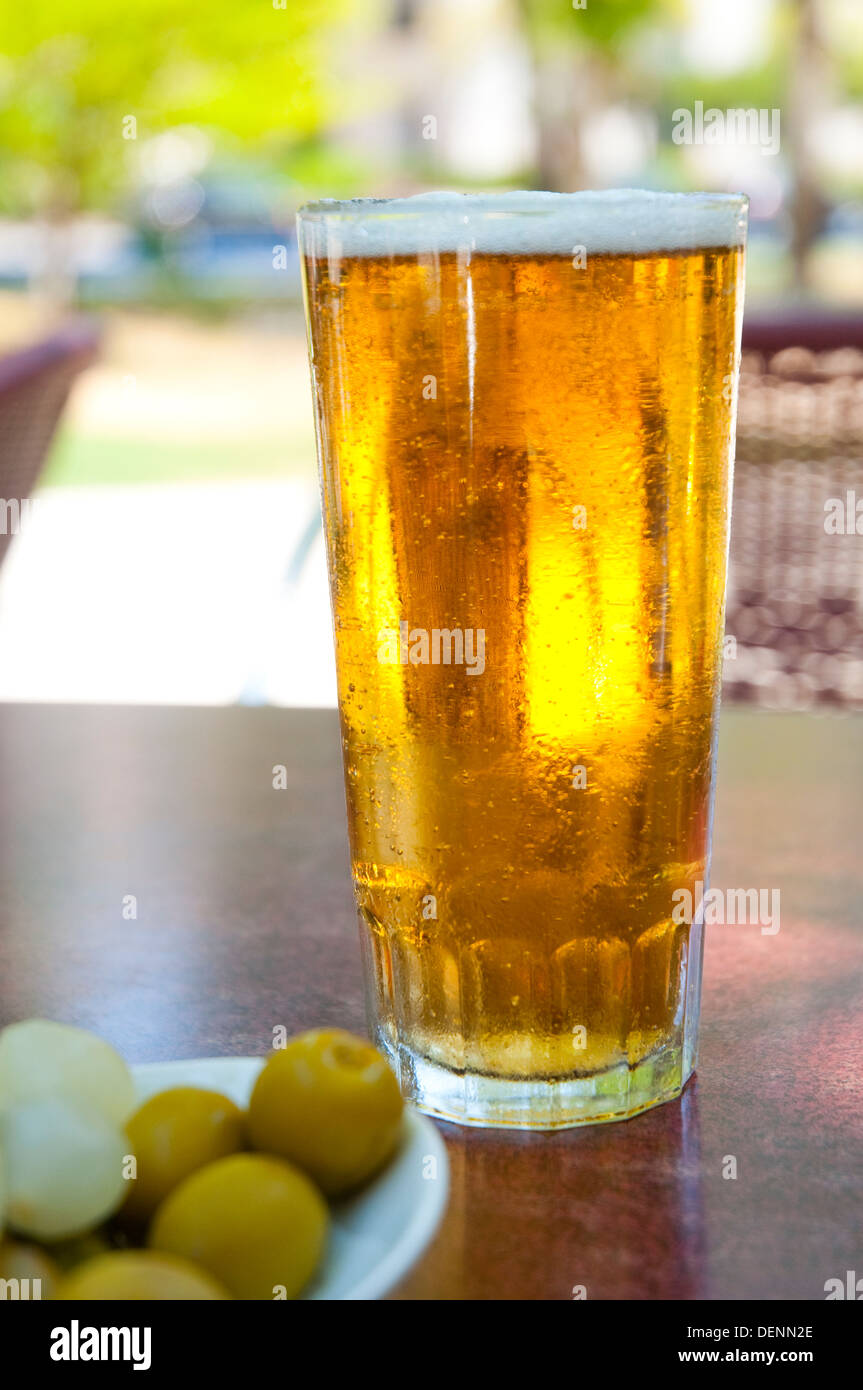 Bicchiere di birra bionda con olive verdi in una terrazza. Chiudere la vista. Foto Stock