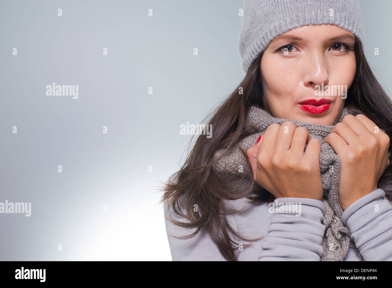 Piuttosto giovane donna in inverno fashion cuddling giù all'interno di lei di lana grigio in maglia jersey, sciarpa e cappello in un freddo giorno Foto Stock