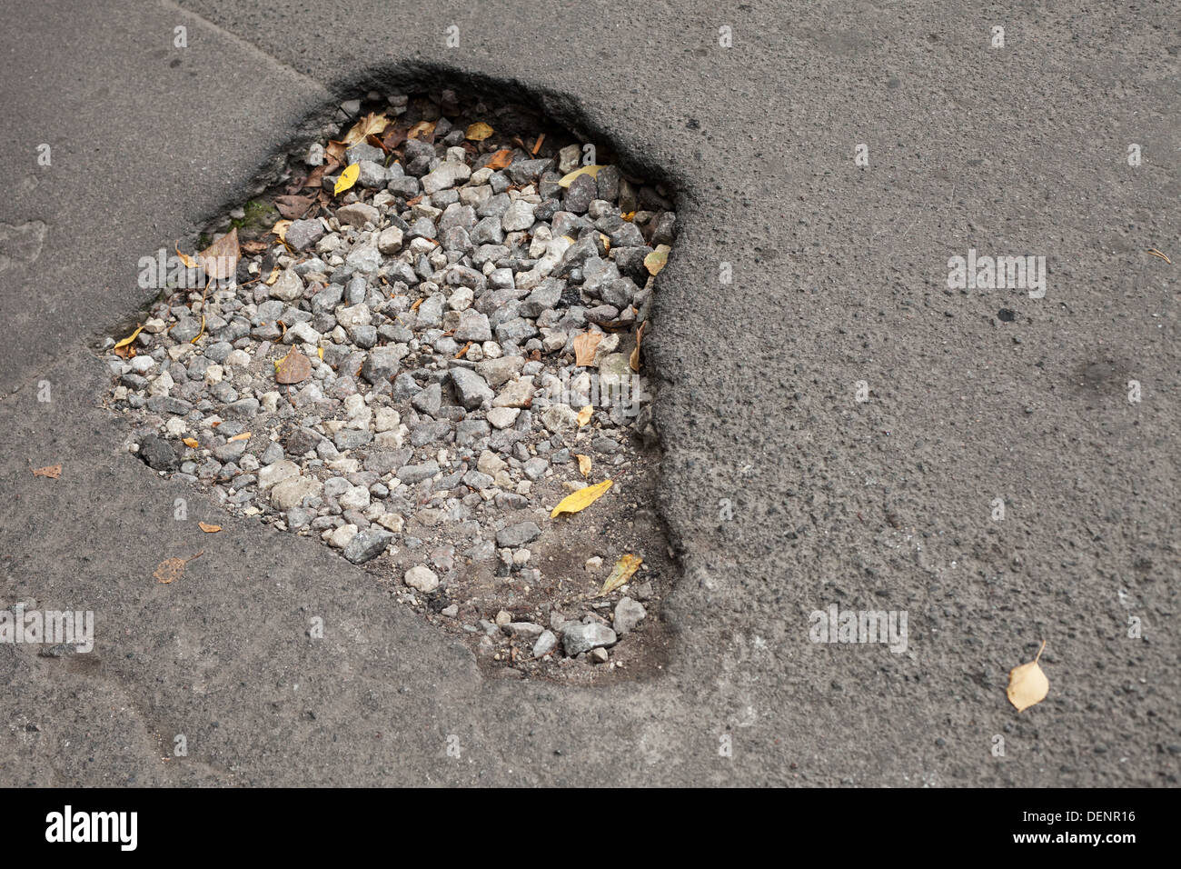 Buca con ghiaia sul danneggiato urban strada asfaltata Foto Stock