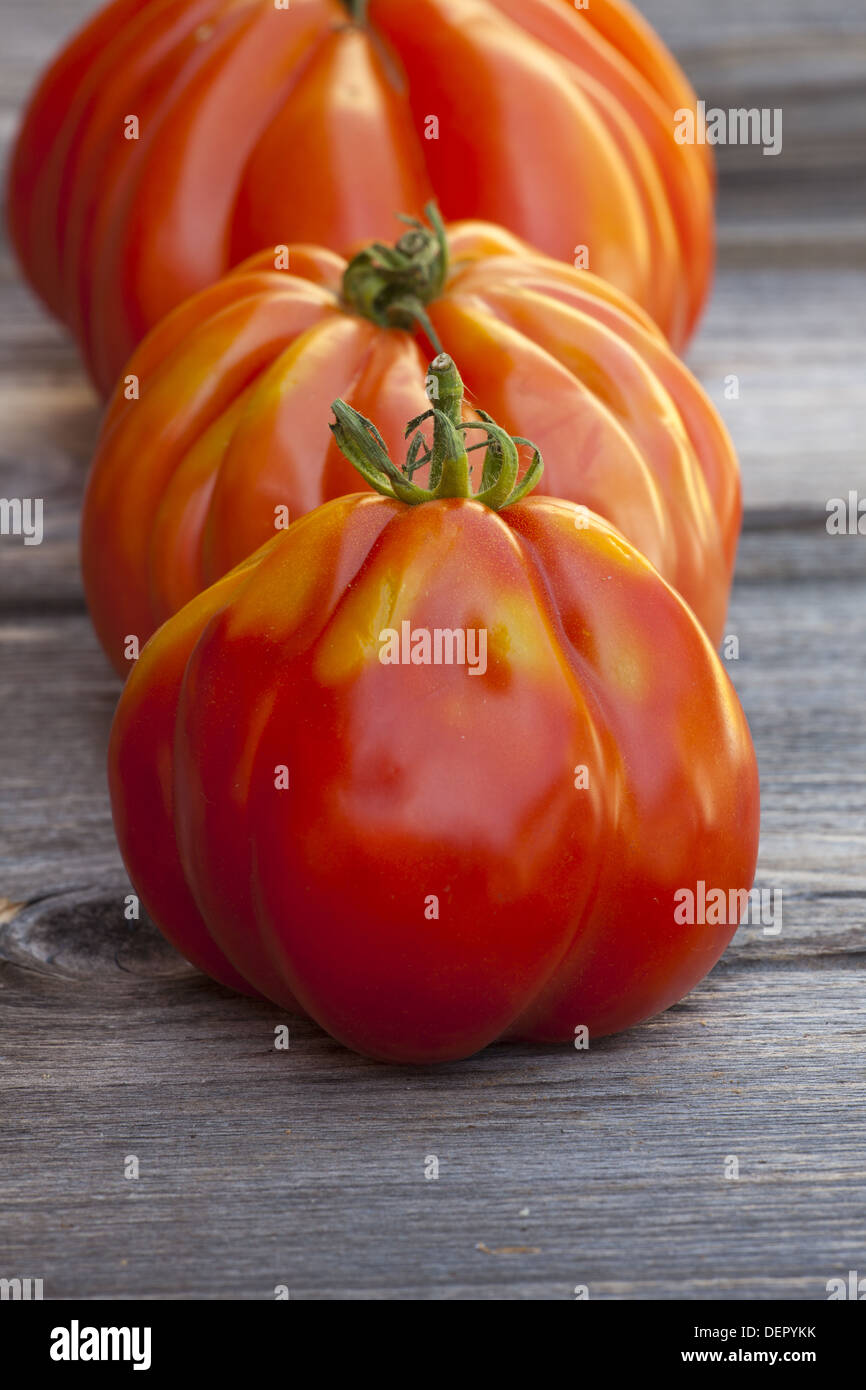 Tre grandi bistecca di manzo pomodori in una fila fresco dal mercato settimanale su un vecchio tavolo in legno Foto Stock