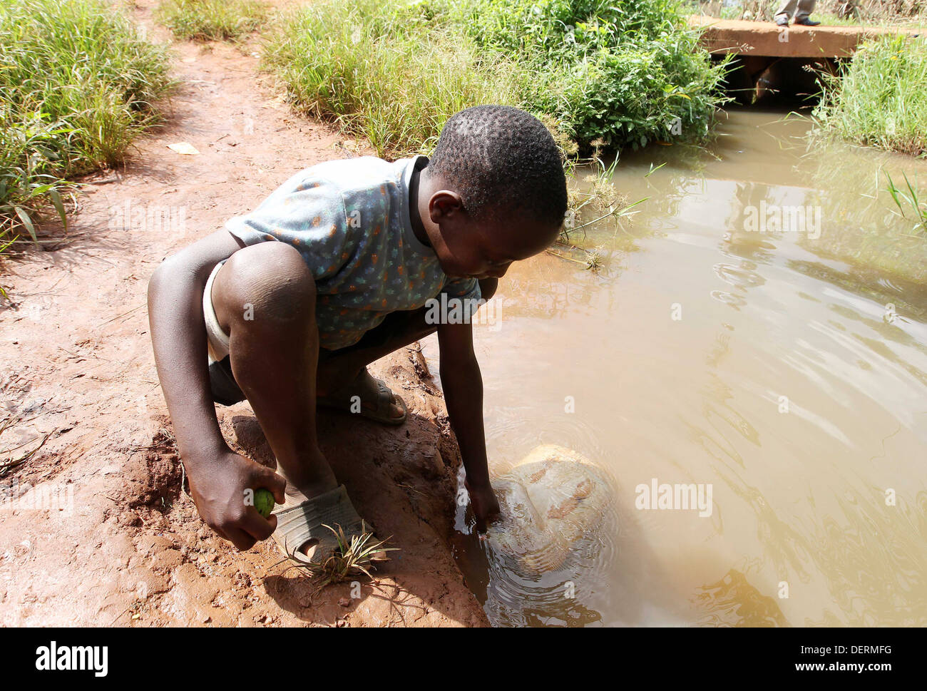 Un giovane ragazzo raccoglie acqua sporca da un fiume nel distretto di Luwero dell Uganda. Foto Stock