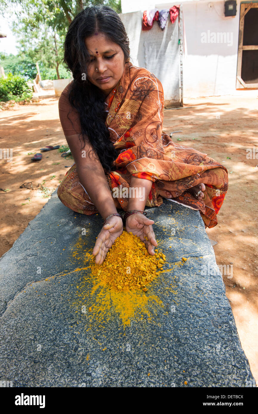 Donna indiana di frantumazione radici di curcuma in polvere in una zona rurale villaggio indiano. Andhra Pradesh, India Foto Stock