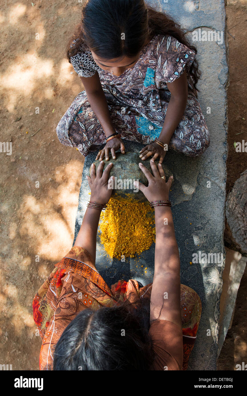 Due donne indiane la frantumazione di radici di curcuma in polvere con una pietra rotonda in una zona rurale villaggio indiano. Andhra Pradesh, India Foto Stock