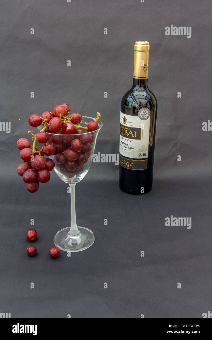 Bottiglia di vino rosso e un bicchiere di uve rosse su sfondo nero Foto Stock