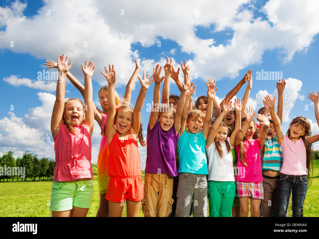 Grande gruppo di bambini, ragazzi e ragazze, 8-11 anni in piedi con volti felici e alzato le mani su soleggiate giornate estive Foto Stock