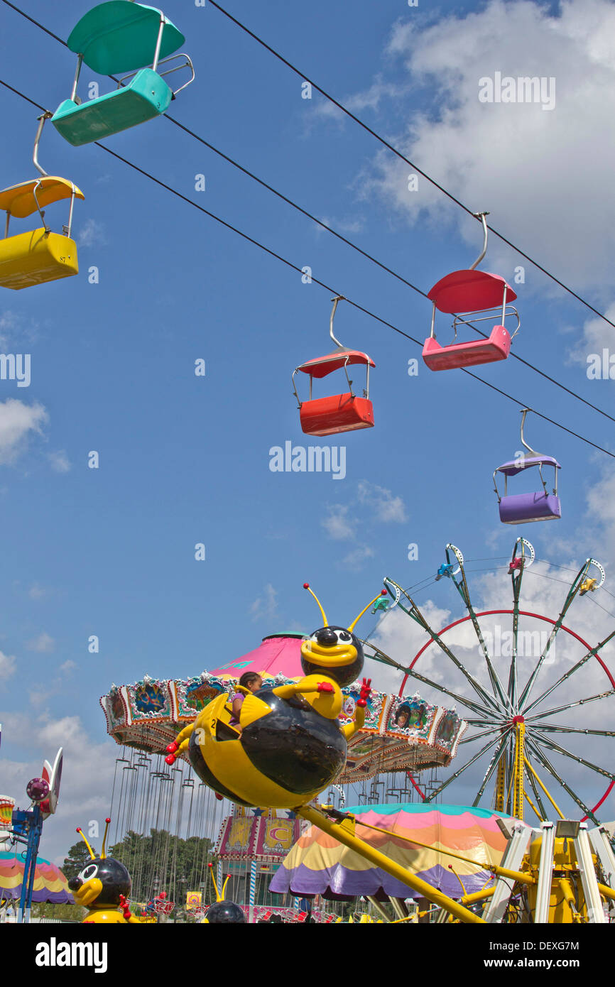 Colorati Tram Sky, una ruota panoramica e un bambino in sella ad una filatura bee ride presso la fiera Foto Stock