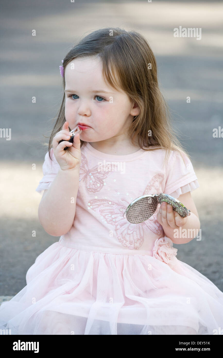 Un grazioso 2 anno vecchia ragazza abito rosa e giocare con il rossetto. Foto Stock