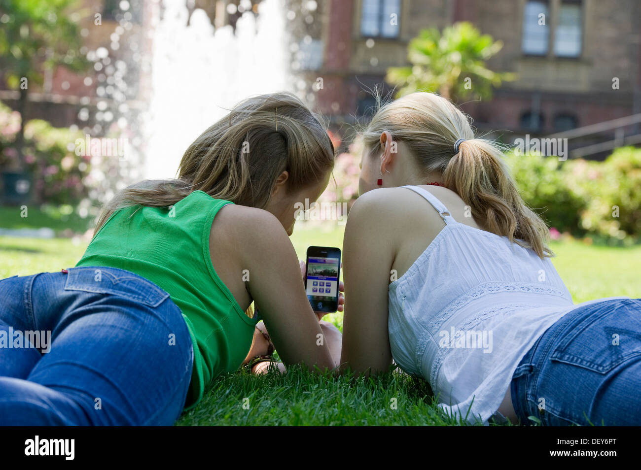 Due giovani donne con uno smartphone, sdraiato su un prato Foto Stock