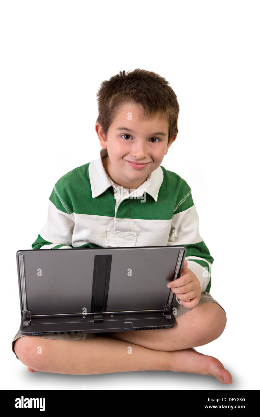 Età elementare ragazzo seduto sul pavimento con le gambe incrociate tenendo il suo laptop forse egli sta lavorando sui suoi compiti o riproduzione di ga Foto Stock