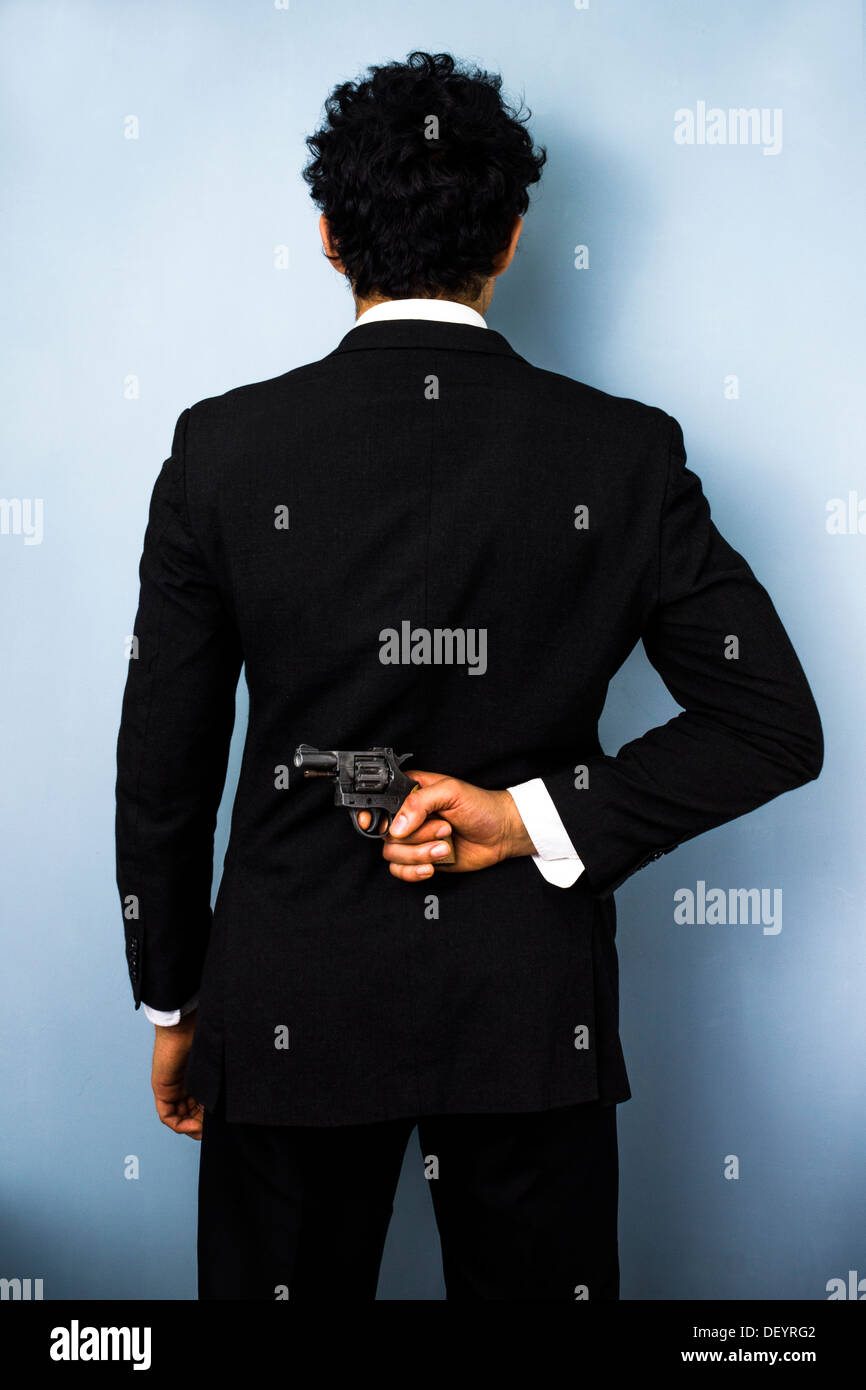 Vista posteriore di imprenditore nasconde una pistola dietro la schiena Foto Stock