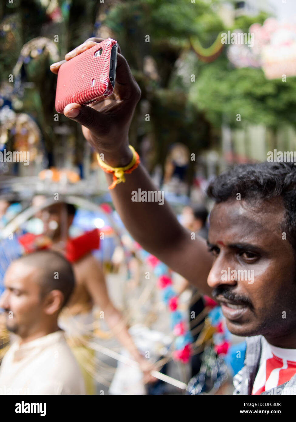 Mano umana utilizza lo smartphone di fotografare la folla si sono riuniti per una processione religiosa in Singapore. Foto Stock