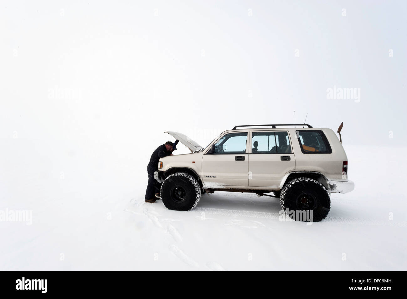 Uomo che guarda nel vano motore con il cofano aperto durante la riparazione di un super jeep in un paesaggio invernale Foto Stock