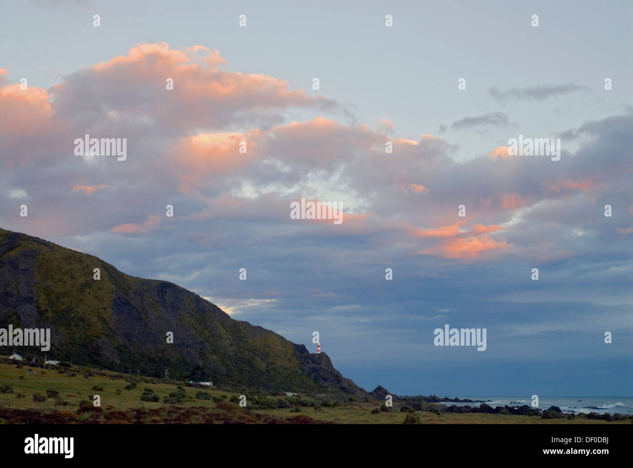 Colorato tramonto nuvole sopra Cape Palliser faro lo stretto di Cook sulla punta meridionale dell'Isola del nord, Nuova Zelanda Foto Stock