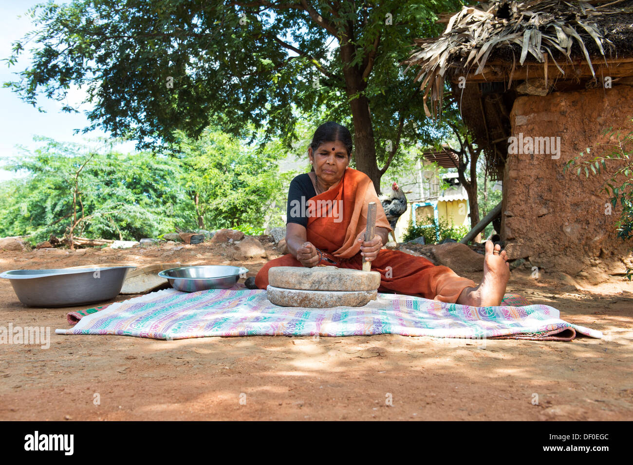Rurale villaggio indiano donna utilizzando pietre Quern per macinare il miglio di dito seme / Ragi semi in Ragi farina. Andhra Pradesh. India Foto Stock