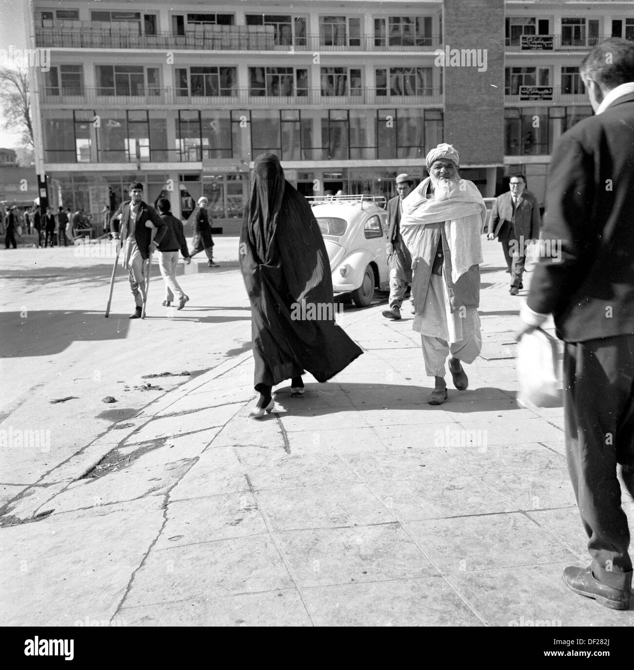 1950, immagine storica di J Allan Cash di un anziano maschio afghano che cammina accanto a una signora completamente velata in una strada a Kabul, Afghanistan. Questa era era un periodo relativamente pacifico per il paese, che ha visto costruire una serie di nuovi edifici moderni, come si vede nel quadro e gli sforzi compiuti per la modernizzazione e rendere il paese una società più aperta e prospera. Questo è giunto alla fine negli anni '70 con invasioni, colpi di stato e guerre civili. Foto Stock