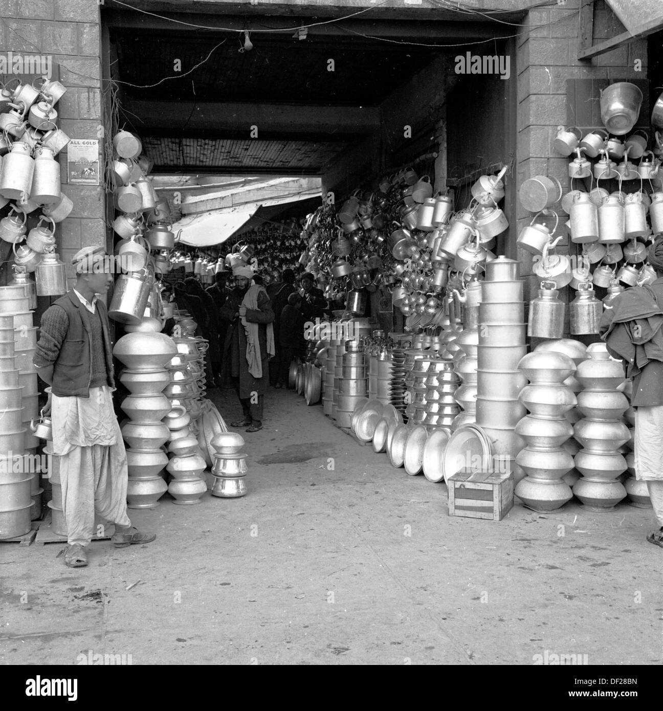 Foto storica,1950 da J Allan Cash, di un giovane maschio afghano in piedi da una bancarella di mercato coperto di strada o bazar in Kabul, Afghanistan, dove una grande varietà di barattoli di metallo, pentole e padelle sono in vendita. Foto Stock