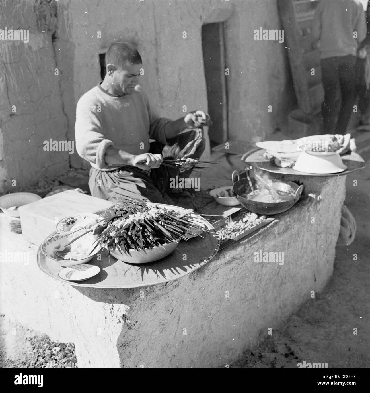 Foto storiche da Afghanistan, anni cinquanta da J Allan contante del commerciante locale a sua stufa, una cucina afgana, preparare il suo cibo. Foto Stock