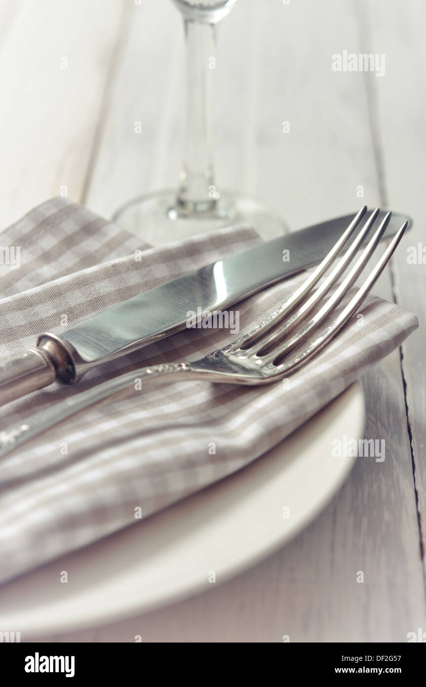 Piastra bianca, coltello e forchetta sulla luce sullo sfondo di legno. Foto Stock